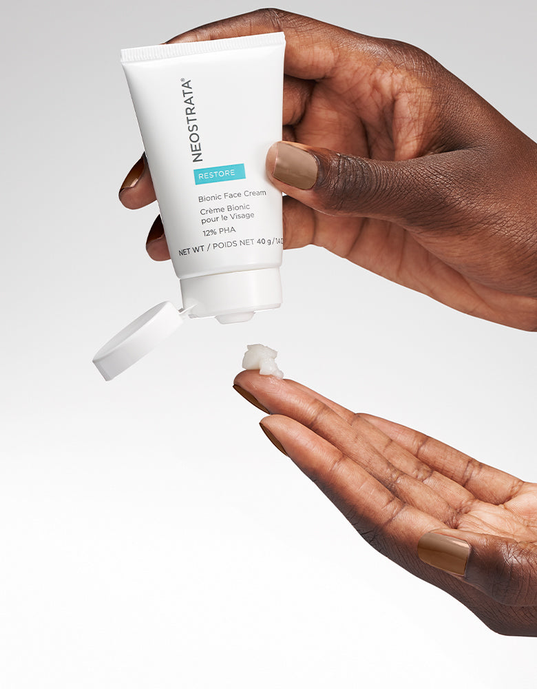 Pair of hands holding a bottle of Neostrata Bionic Face Cream against a white background.